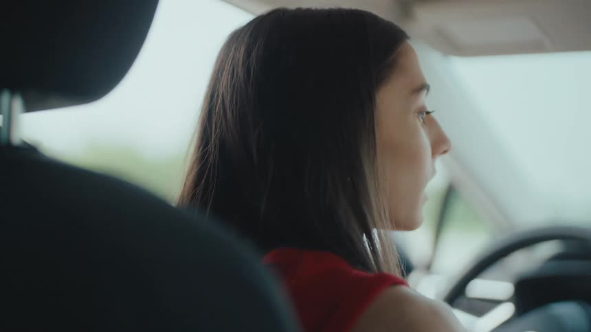 A young woman is driving a car turning the steering wheel as she navigates the road at midday