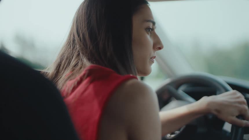 A lady driving looks at the side mirror while making a turn at daytime