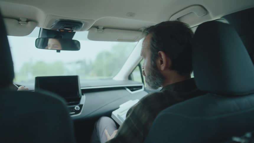 A bearded man sits in the passenger seat while a woman drives a car