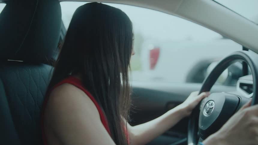 A woman wearing a red dress with long hair drives a toyota car in the middle of the day