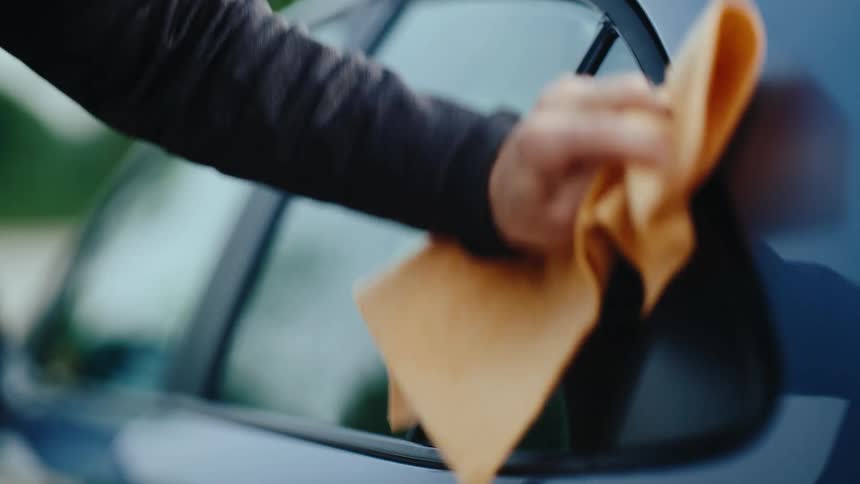 A hand wipes a car window clean with a cloth