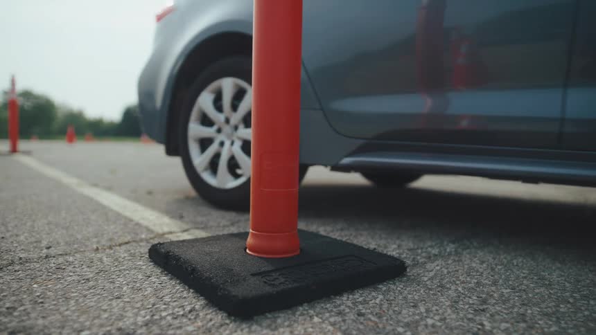 From a lowangle perspective a car slowly pulls alongside an orange traffic pylon to park during a driving test