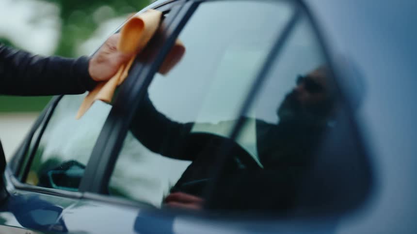 Person cleaning a car window with a cloth while another person is visible inside the car