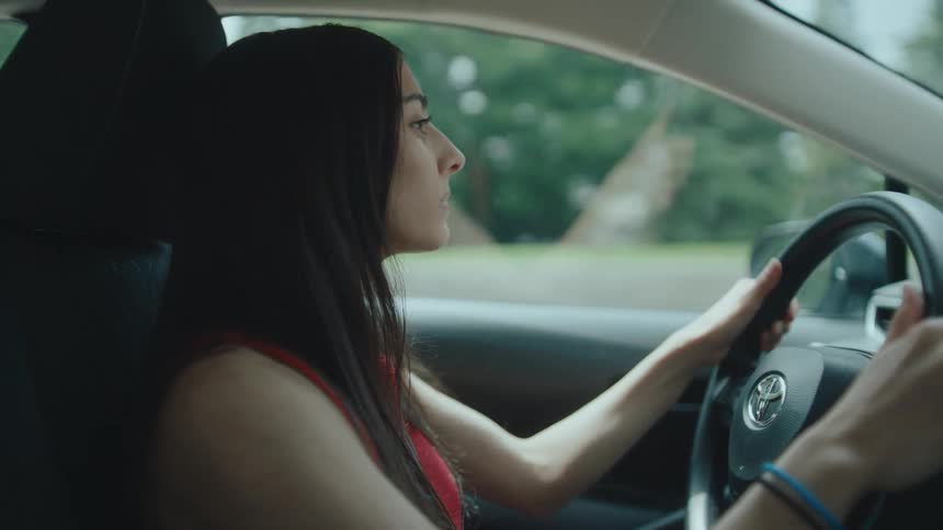 A young woman with long black hair is driving her toyota car on the highway at midday