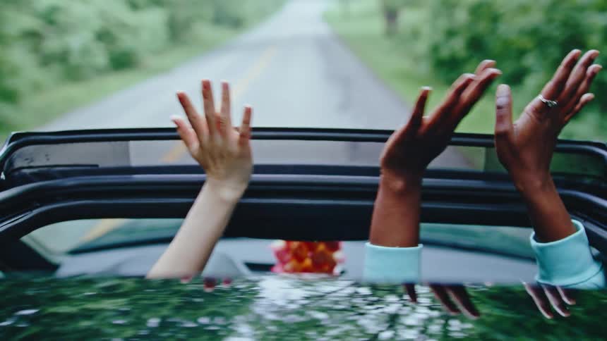 Hands waving out of sunroof while driving on a tree lined road