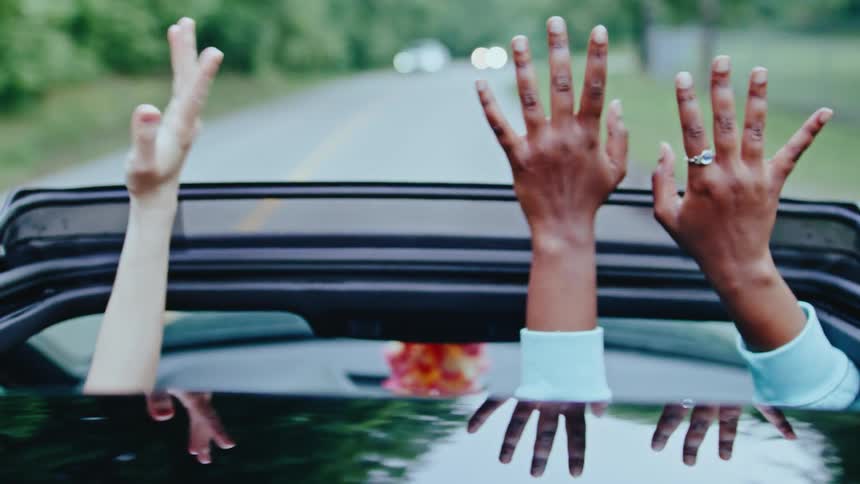 Hands waving out of sunroof while driving on a tree lined road