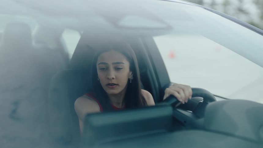A woman driving a car looks forward with a concerned expression