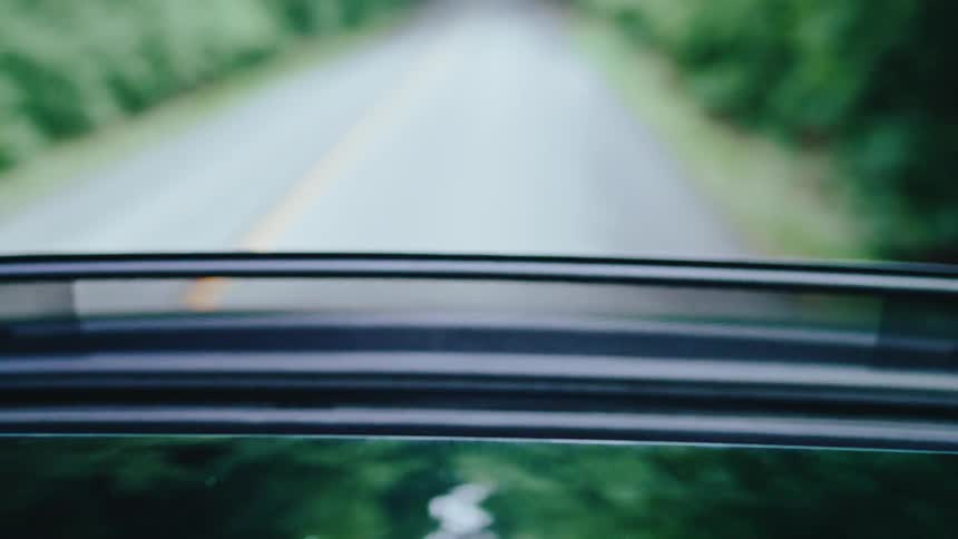 Pair of hands of a person appearing through the sunroof of a moving vehicle