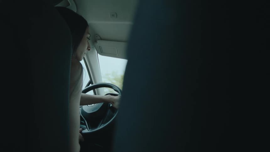 A young woman turns the steering wheel as she drives her vehicle along a road