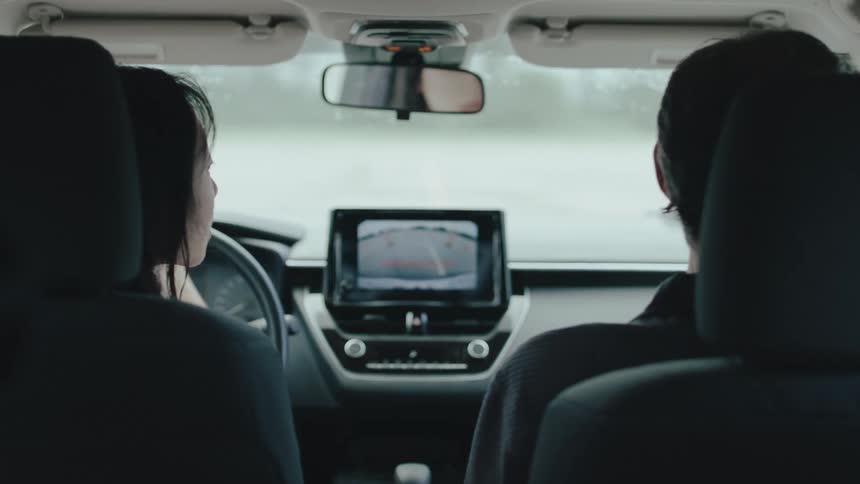 This video shows the interior of a car from the back seat with two people in the front seats the camera focuses on the dashboards screen which displays a map while the drivers hands briefly adjust the steering wheel