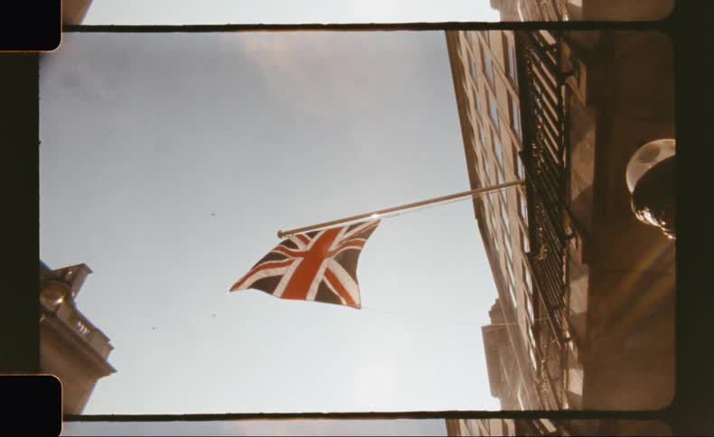 A union jack flag flutters on a sunny day in front of a city building