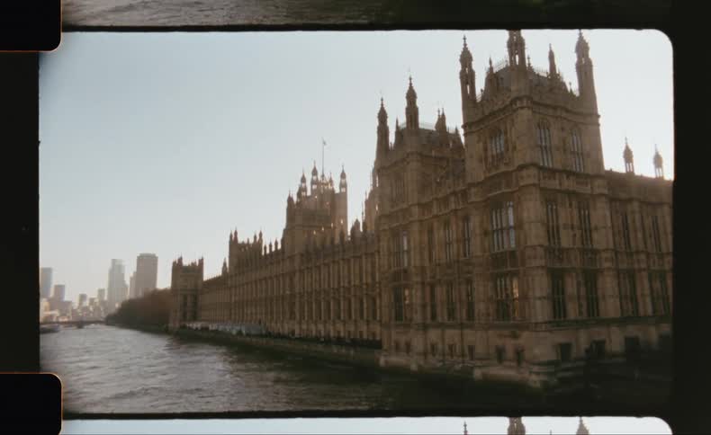 The palace of westminster stands beside the river thames framed by modern highrises and a partially cloudy sky