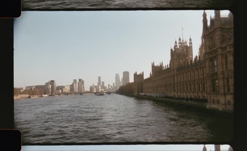 The palace of westminster lines the right bank of the river thames as boats pass under a cloudy london sky