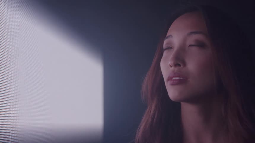 A young woman with red hair stands beside a bright screen and as the screen shuts off the room becomes completely dark