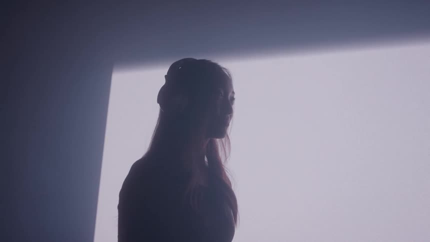Woman stands alone in dramatic moody lighting against a bright wall