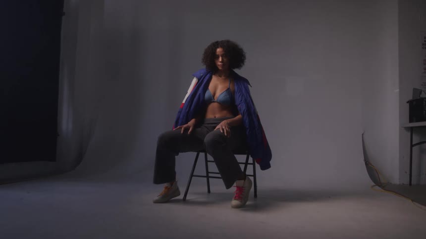 Curly haired woman wearing fashionable outfit sitting on a chair posing in a studio