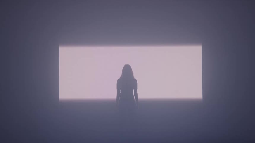A lady stands in a very dark room as a sudden burst of bright light reveals her presence casting sharp shadows around her