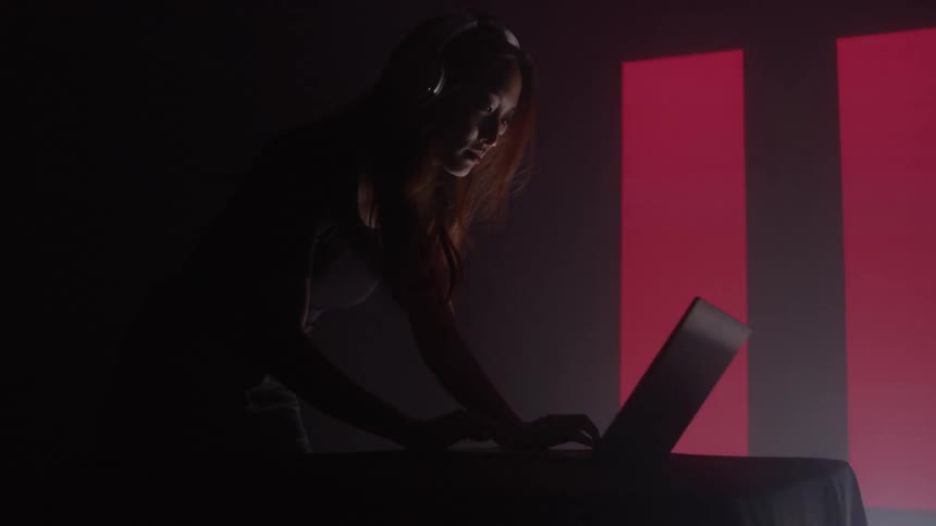 A dj performs under moody lighting beside a glowing red symbol