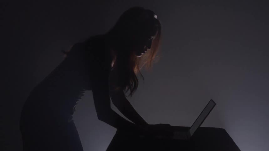 A woman types on a laptop in front of a glowing red screen