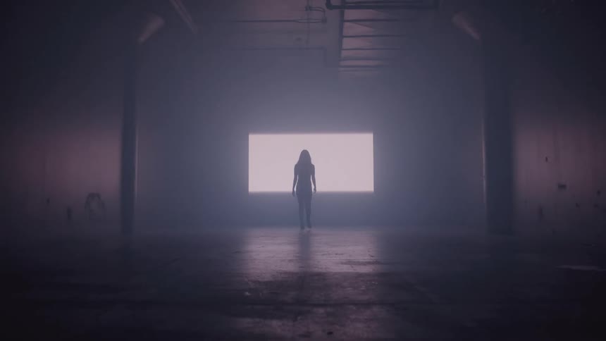 A woman walks through an empty room toward a growing light on the wall