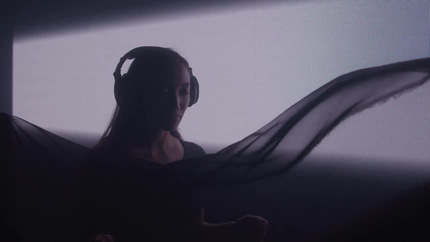 Woman with eyes closed wearing headphones in a dark room with a screen next to her