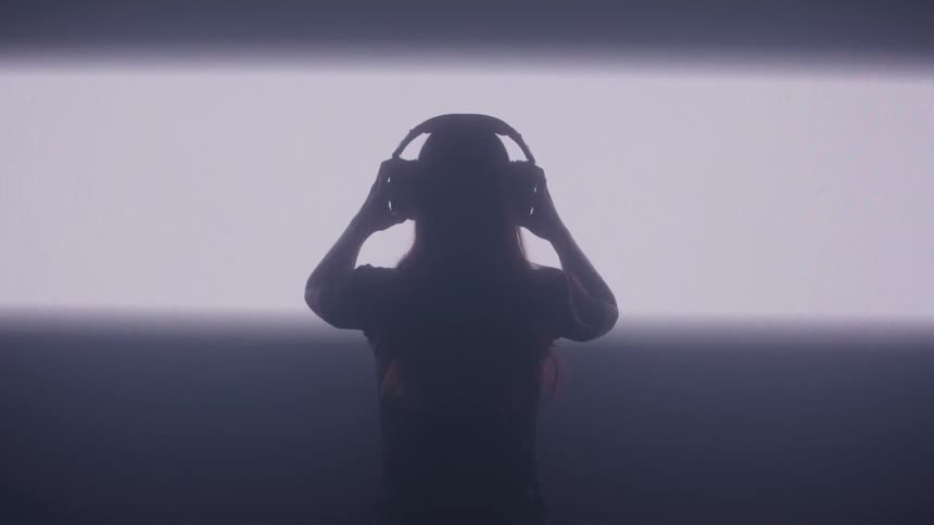 A silhouette stands in front of a single horizontal beam of light in a dark room modeling headphones