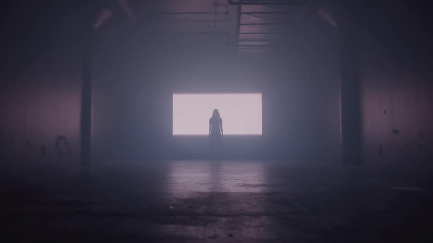 Light spreads on the wall in front of the woman in the foggy room