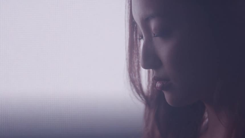 A young asian woman looks downward in a room as a bright light shines