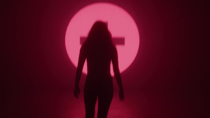 Woman silhouetted by displayed symbols walks through the dark towards those symbols