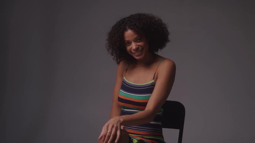 A woman in a striped dress laughs while seated in a photography studio