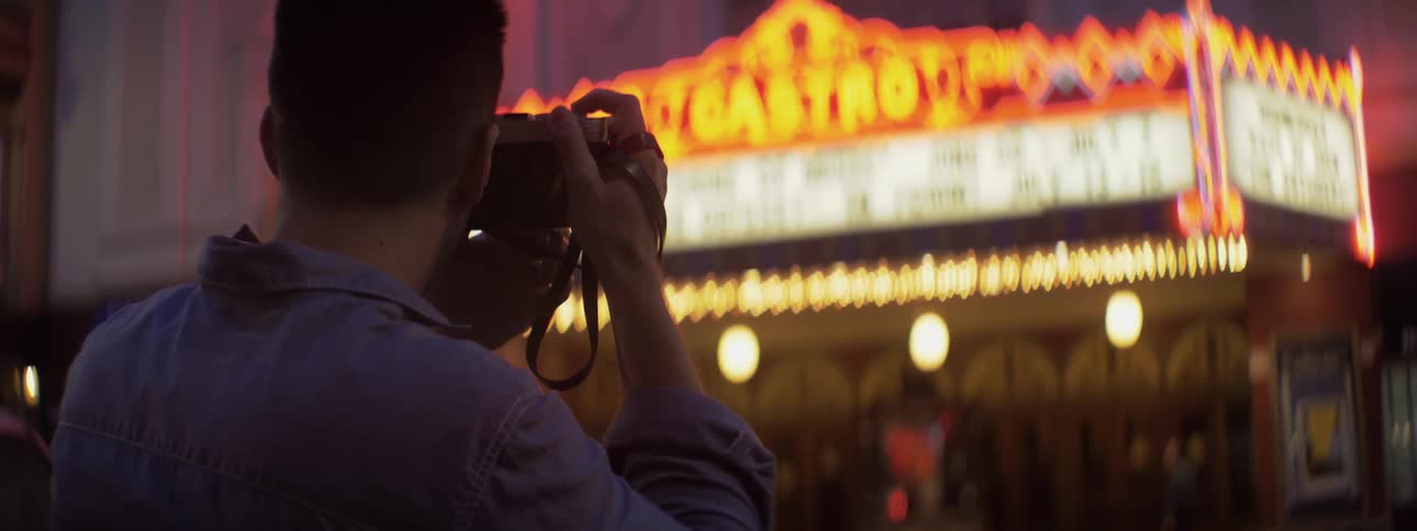 A man takes a photograph of a lit billboard sign
