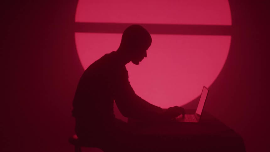 The man types on his laptop as symbols flash on the wall