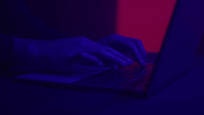 Hands type on a laptop in moody red lighting