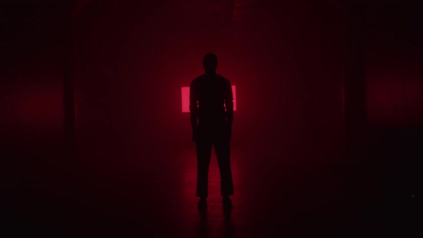 The man is watching the flashing red symbols on the wall in the dark room