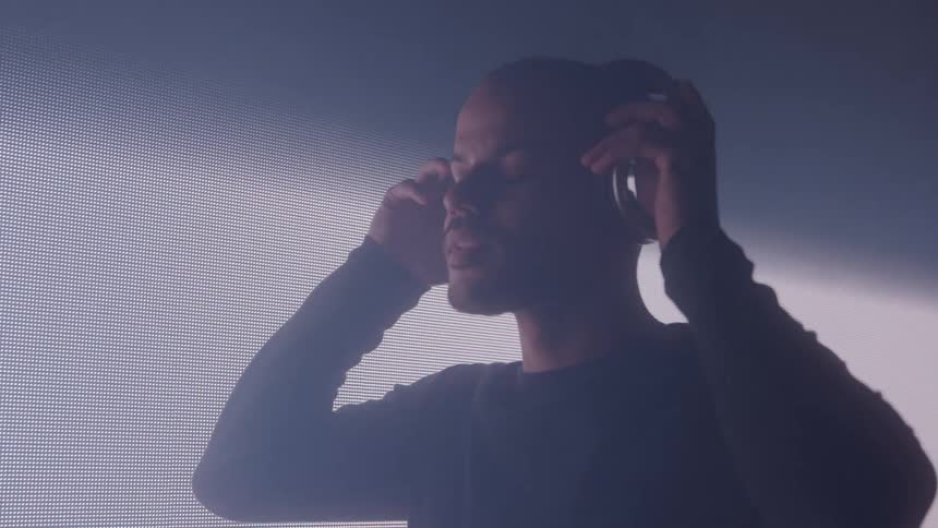Man with eyes closed putting on headphones in a lighting fitting room with a screen next to it