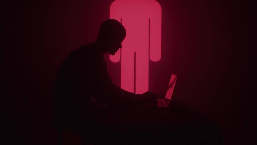 A shadowy figure silhouetted against a dynamic backdrop of changing red and pink lights is intensely focused on a laptop various graphic symbols like a triangle a circle and an exclamation mark appear and disappear on the wall behind them