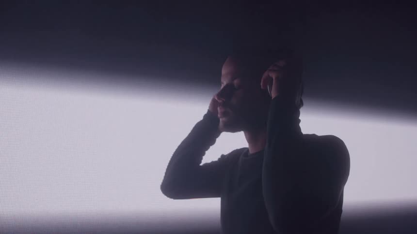 A man closes his eyes while placing headphones over his ears