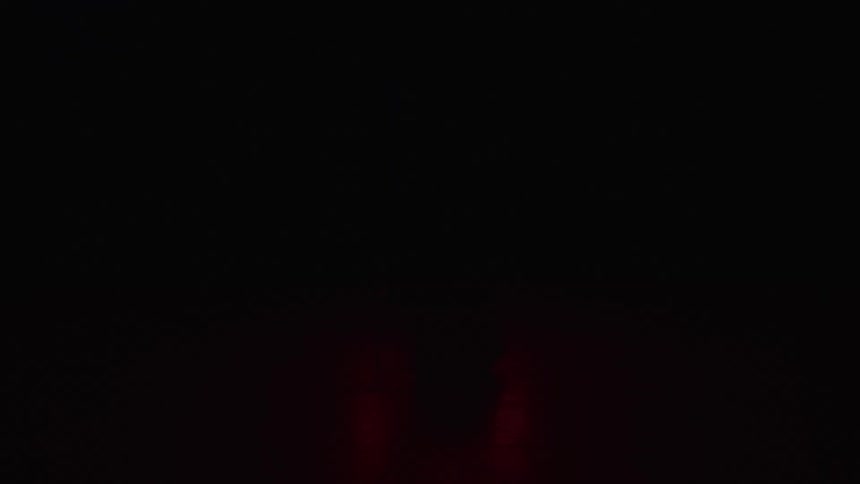 A silhouetted figure works at a desk before a glowing red triangle in a dark room