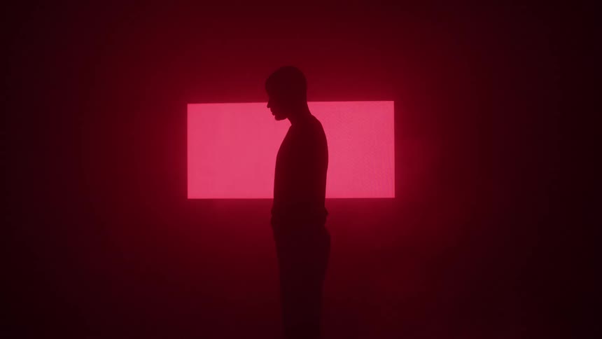 A man is standing in a dark room as flashing symbols are displayed on the wall