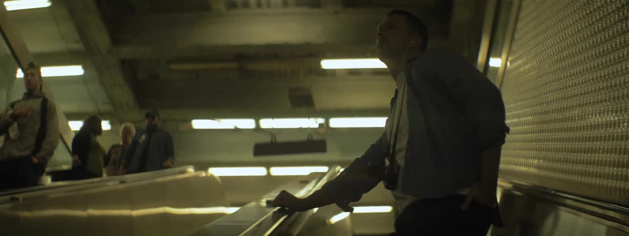 A man wearing headphones rides an escalator