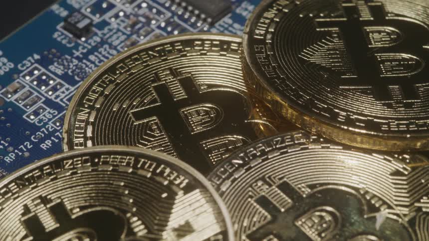 Multiple coins imprinted with the bitcoin logo are pile atop a circuit board