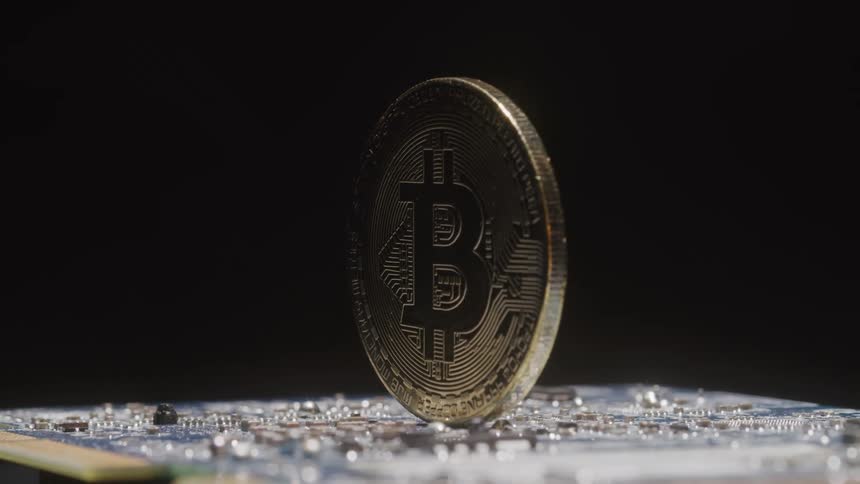 A coin with a bitcoin logo on it is atop a printed circuit board