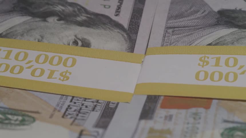 Stacks of 100 bills bound with yellow bands labeled 10000 sit neatly arranged on a dark surface