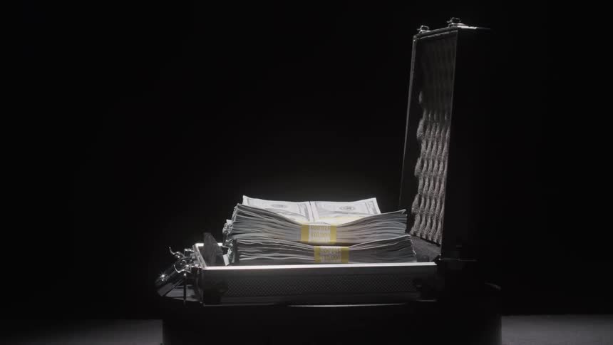 An open metal briefcase packed with neatly stacked bundles of cash rests on a dark surface