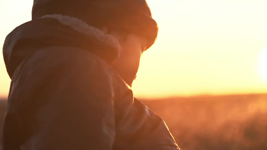 Woman stands and looks towards the ground at sunset