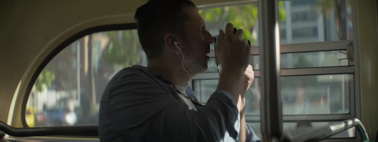 A man holding a camera takes photos as he rides on a bus