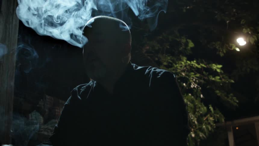 A man smokes a cigar outside at night