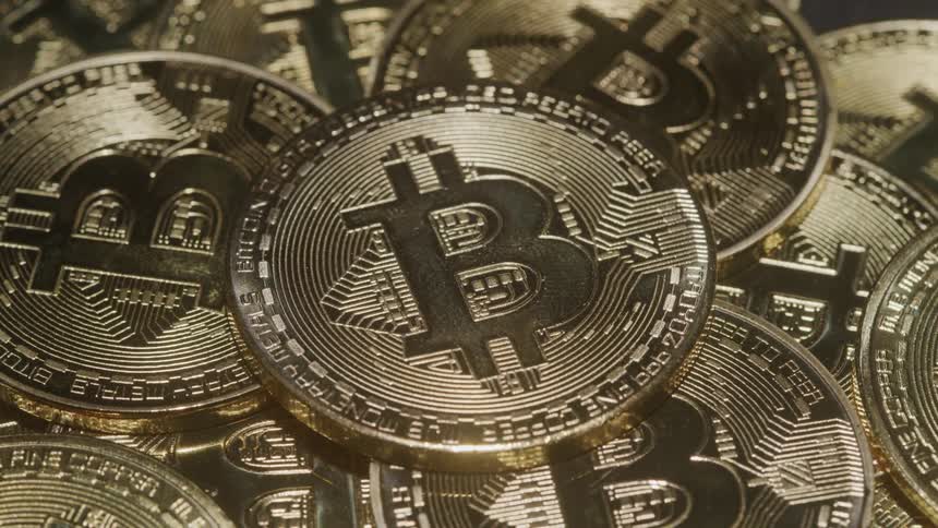 A cluster of gleaming golden bitcoins fills the frame with one prominent coin in the foreground catching the light the detailed texture and metallic sheen of the coins are clearly visible highlighting their symbolic value as digital currency