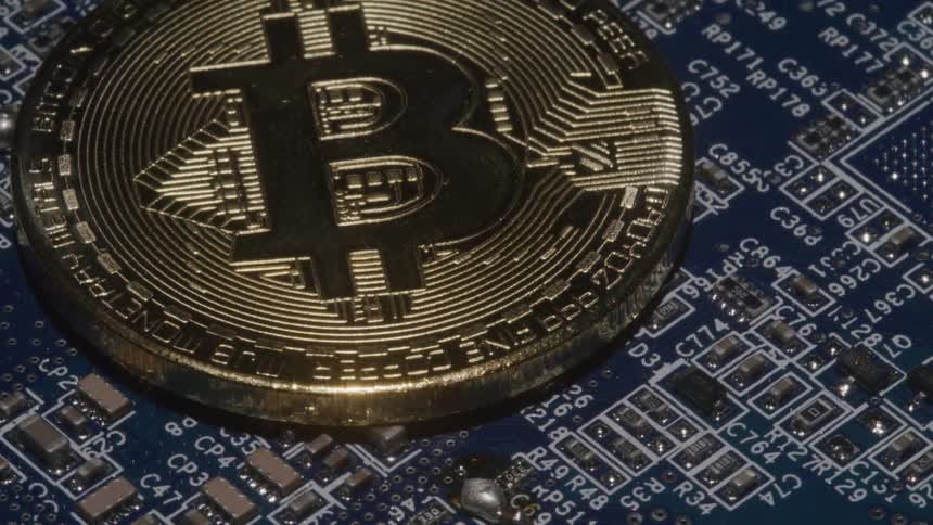 A gold bitcoin sits on top of a detailed blue computer circuit board