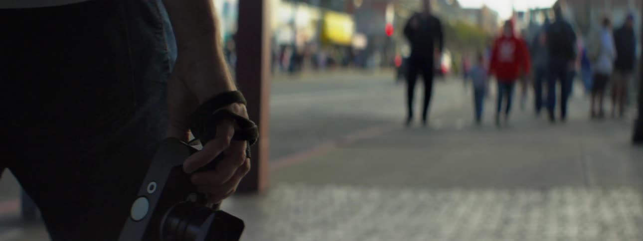 A man walks down a city sidewalk with a camera in hand
